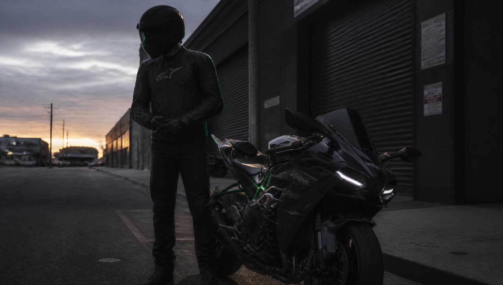 Motorcycle rider in full protective gear beside a sport motorcycle at dusk
